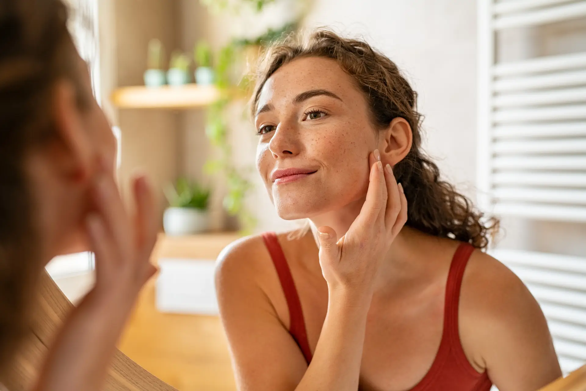 Young woman checking her skin at mirror in the morning