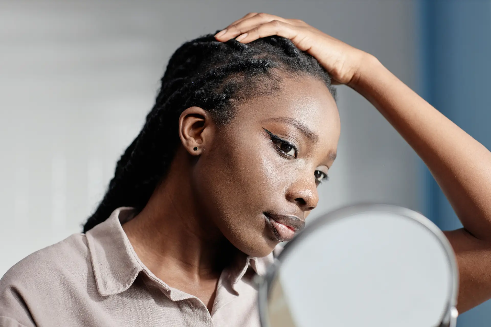 Woman Touching Hair Looking in Mirror during Self Care Routine in Bathroom