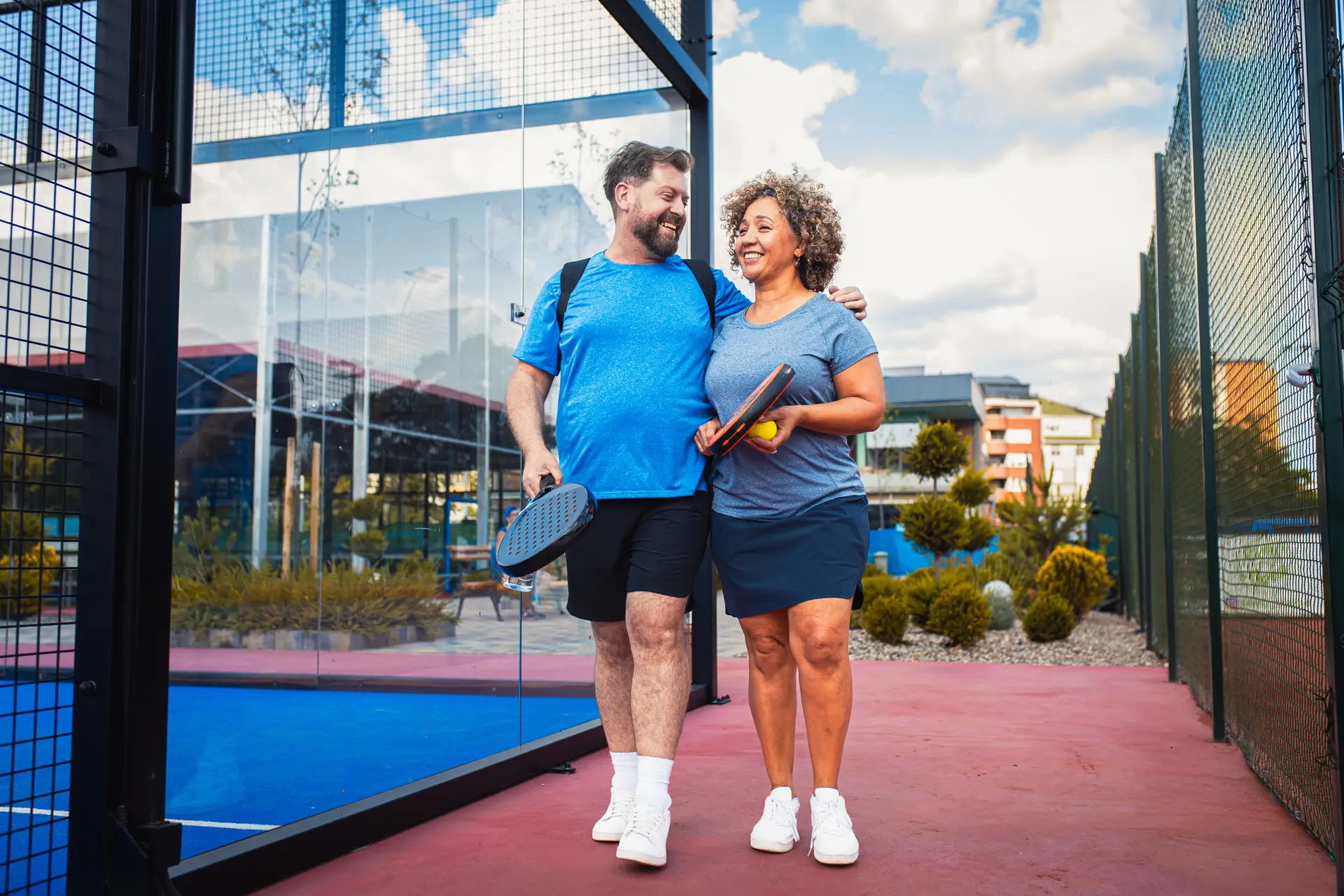 Smiling mix couple comes to the outdoor court to play pickle ball